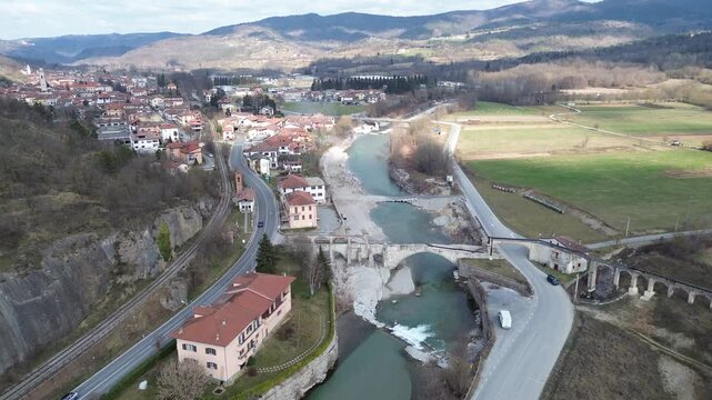 Aerial drone footage of a serene river winding through the lush springtime plains of Piedmont near Cuneo province with warm sunlight illuminating the rural Italian countryside and rolling green meadow
