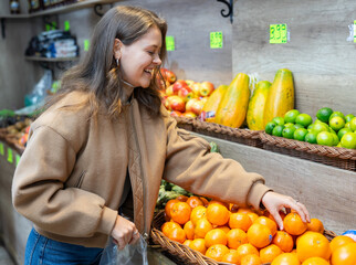 Young woman selects and buys fresh oranges in a grocery store
