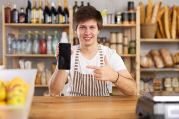 Young male seller showing information on smartphone screen in grocery store