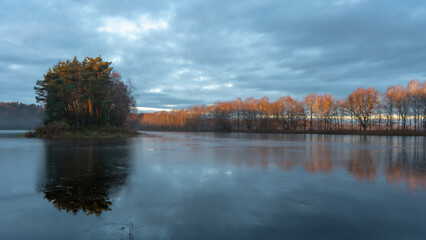 Wschodzące słońce oświetla czubki drzew nad stawem