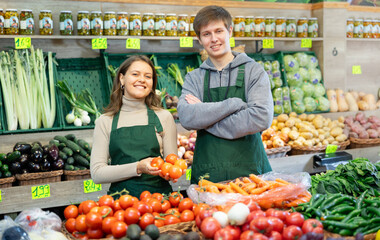 Happy young male and female sellers posing in grocery market with tomatoes in hand