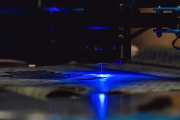 Close up of laser cutting paronite. Powerful blue laser burning complex gasket shape out of asbestos material. Smoke and sparks visible during precise manufacturing of industrial seals.