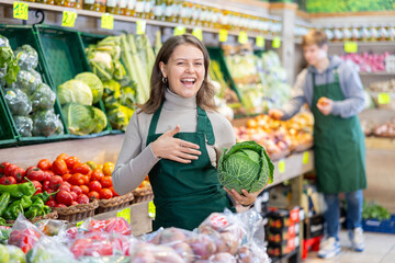 Positive girl seller with cabbage in her hands in the grocery department of the supermarket