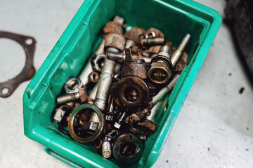 Oily transmission details: broken gearbox unit and green bin with spare parts. Close up of worn out...