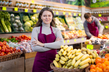Young woman seller in uniform lays out bananas on counter in grocery store..