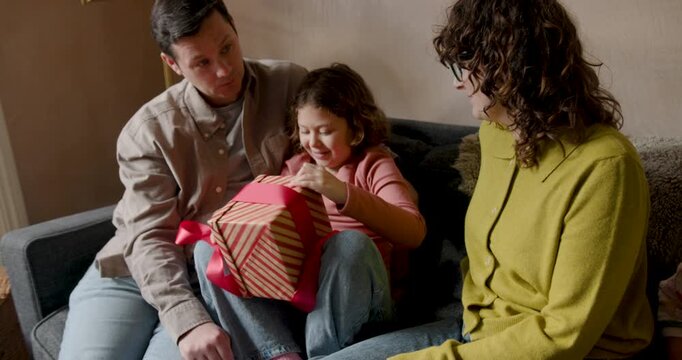 Family at home on Sofa with Child unwrapping Soft Toy in Gift Box