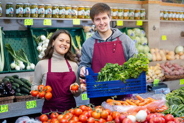 Positive smiling guy and girl sellers offering fresh vegetables in vegetable store