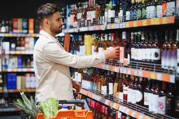 Man choosing wine bottle in modern supermarket liquor aisle