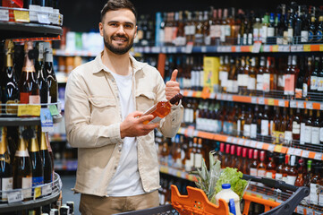 Happy man shopping for wine in supermarket