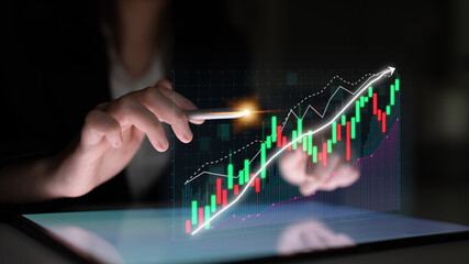 A business professional analyzes financial data on a tablet, with a digital graph illustrating upward trends and projections, representing growth and strategy. Impute