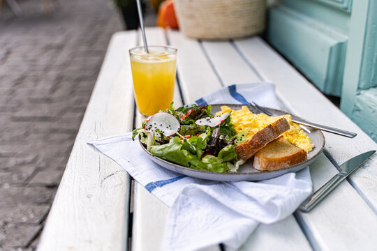 Close-up of a plate of scrambled eggs with toast, salad and a glass of orange juice on a garden table - Powered by Adobe