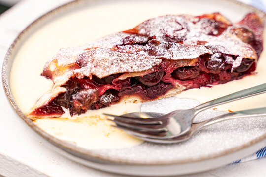 Close-up of a slice of cherry strudel with hot vanilla sauce on a garden table