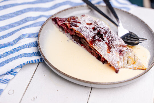 Close-up of a slice of cherry strudel with hot vanilla sauce on a garden table