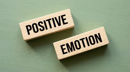 Two wooden blocks with 'POSITIVE' and 'EMOTION' printed in bold black text placed on a textured teal background positive emotion happiness joy feeling mindset thought psychological