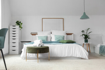 Interior of stylish hotel room with houseplants, ottoman and cozy bed
