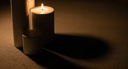Three white candles, one lit, casting long shadows on a textured surface in a dimly lit room, creating a warm and contemplative ambiance.