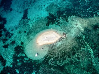Tiny sandbar island with boats anchored in turquoise reef lagoon