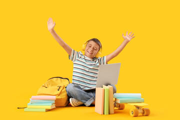 Little boy in headphones with laptop studying computer sciences on yellow background