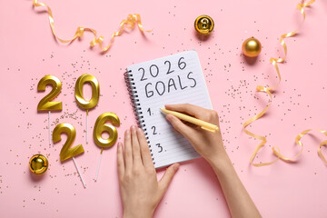Woman with candles in shape of figure 2026 and Christmas decor writing to-do list on pink background