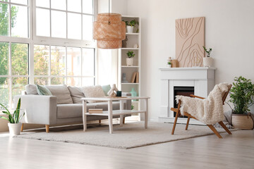Fototapeta premium Fireplace, table sofa and armchair in interior of light living room