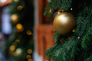 Golden Christmas bauble on fir tree with festive lights and soft bokeh