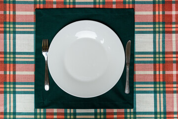 White plate and cutlery on green placemat over plaid tablecloth