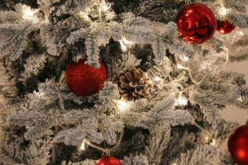 Snow-covered Christmas tree decorated with red baubles, a pine cone, and warm string lights, creating a festive holiday and winter atmosphere.