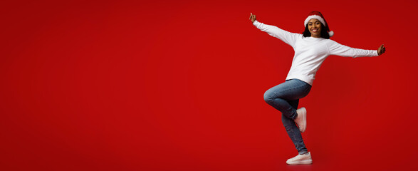 A woman wearing a festive Christmas hat dances with enthusiasm on a vibrant red background. Her joyful expression reflects the spirit of the holiday season.