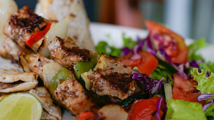 Close-up of grilled meat skewers with vegetables, fresh salad, tomato, purple cabbage and lime. Vibrant colors, shallow depth of field, perfect for food, menu, restaurant and healthy-eating themes