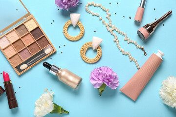 Makeup products with accessories, flowers and confetti on blue background