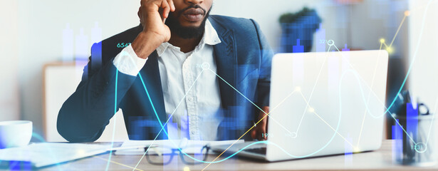 In a contemporary office setting, a focused African American businessman engages in a phone call while skillfully working on his laptop.