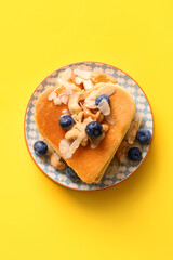 Plate with tasty pancakes in shape of heart, blueberry and nuts on yellow background. Valentine's Day celebration