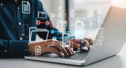 Close up of a man typing on silver laptop with digital file icons, symbolising the data being transferred, displayed on a white tabletop under soft lighting.