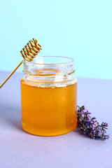 Jar of sweet lavender honey, dipper and flowers on lilac table