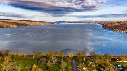 Obraz premium Autumn, fall, panorama aerial, drone, photo over Cayuga Lake, Ithaca, NY. Clouds reflecting on calm water surface. November 2025