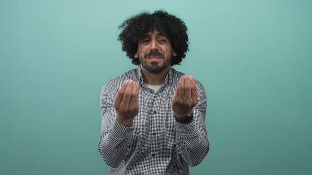 Man with curly hair showing cupped hands begging gesture in mint green studio; pleading request empathy.