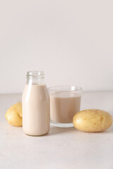 Bottle and glass of tasty potato milk on light background