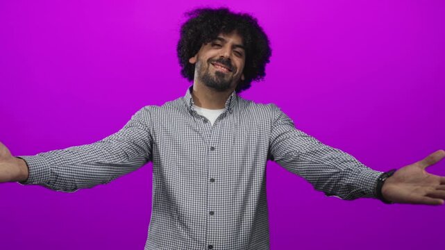 Man with curly hair clasping hands to chest in a studio with vivid purple backdrop; gratitude warmth connection.
