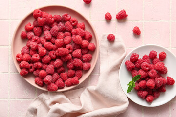 Plates with fresh raspberries on pink tile background