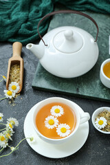Cup of hot chamomile tea and teapot on black background