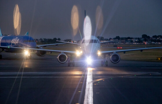 Front view of an Embraer regional jet with bright lights on taxiway at dusk at Boston's Logan International Airport - Boston, Massachusetts, USA