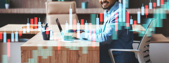 A cheerful businessman works on his laptop at a sleek office desk, managing emails and browsing the web. The modern interior and his smile reflect productivity and success in his career.