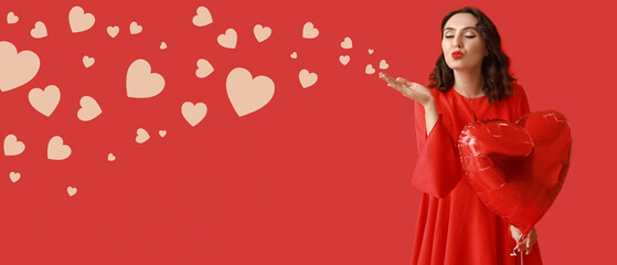 Beautiful young woman with heart shaped air balloon blowing kiss on red background