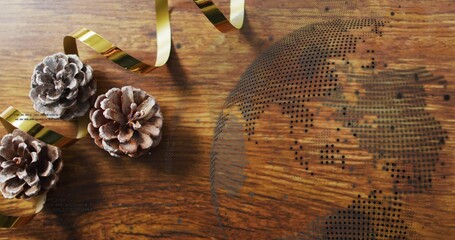 Clustering three frosted pine cones with metallic gold ribbon on warm wooden tabletop, dotted globe