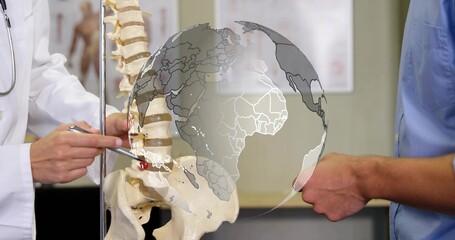 Pointing doctor in lab coat with stethoscope indicating vertebra on spine model in clinic, globe