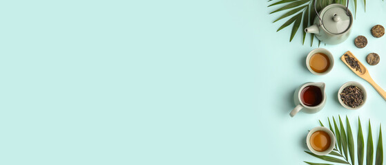 Composition with teapot, cups, dry pressed tea and tropical leaves on light blue background with...