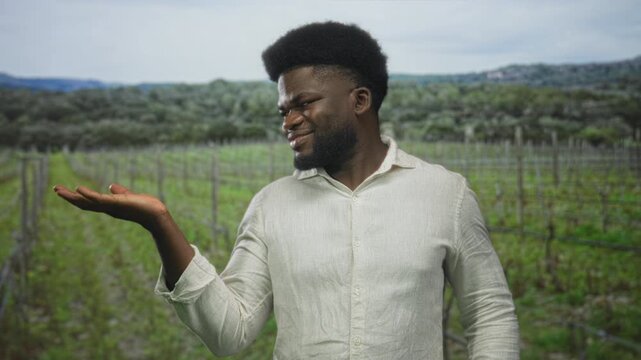 Man holding palm up in a forest vineyard while smiling and presenting with hand visible, wearing light shirt; contentment.