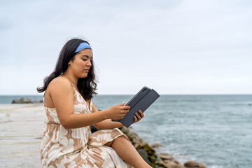 Young woman enjoying digital reading by ocean waves