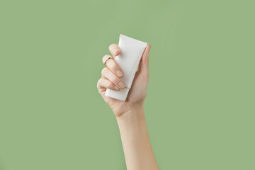 A womans hand holding a white cosmetic tube on a green background