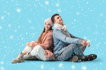 Happy couple in winter clothes sitting on blue background with snow